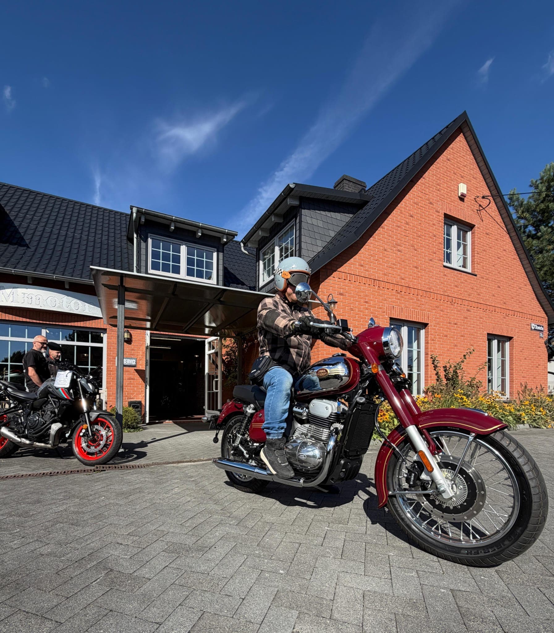 Motocyklista na bordowej Jawie 350 CL przed salonem MotoJawa