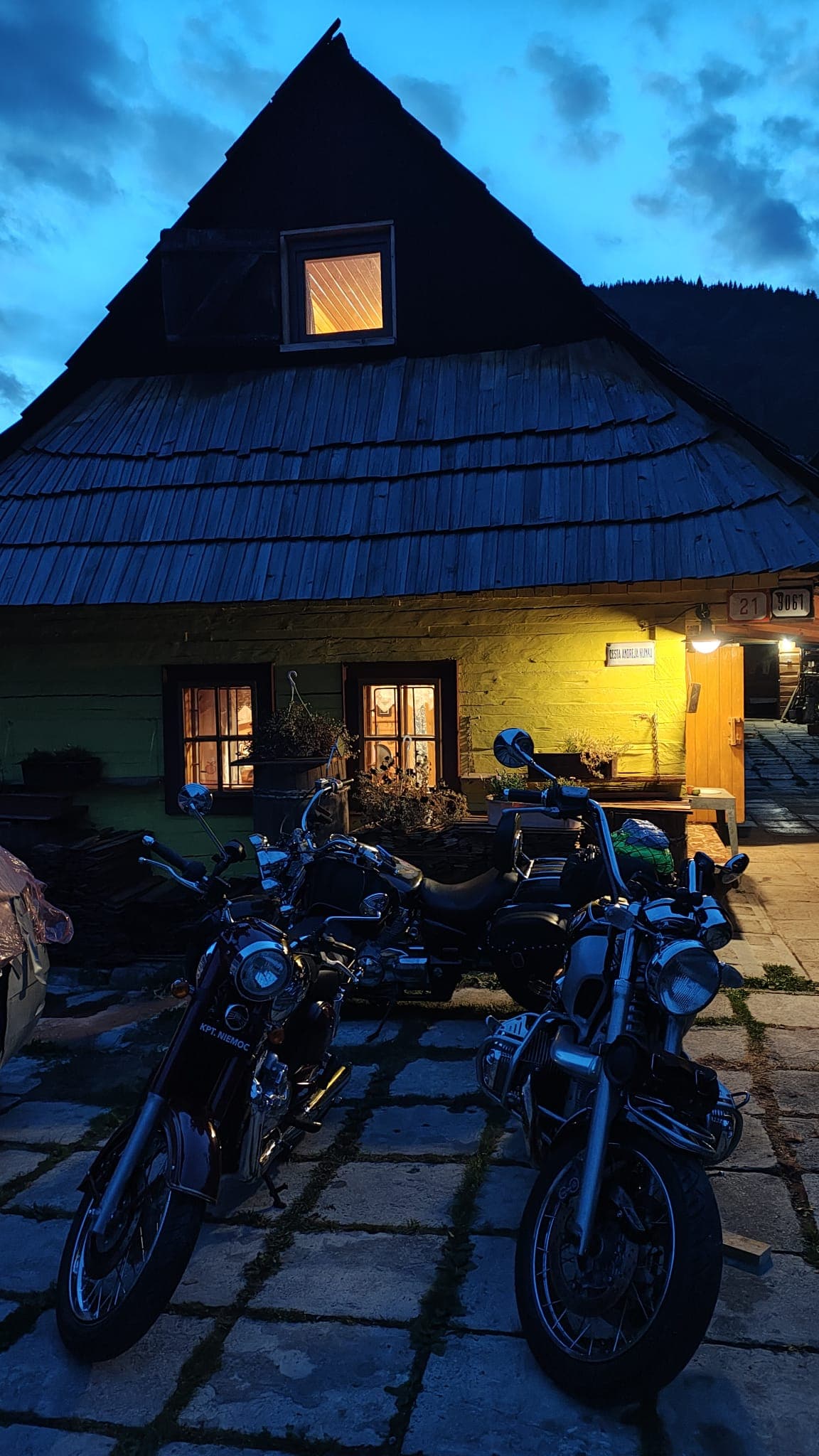 Motocykle zaparkowane nocą przed oświetloną drewnianą chatą w Vlkolíncu